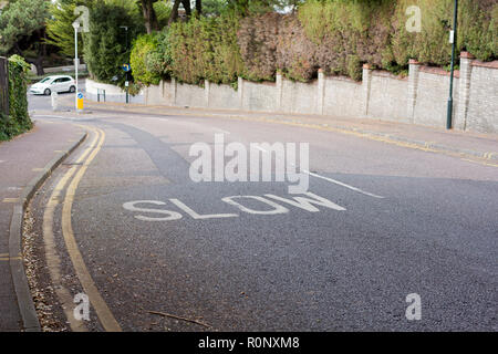 Slow warning sign painted in white on road surface, next to double yellow lines, United Kingdom Stock Photo