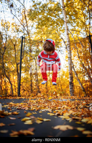 Boy jumping on a trampoline covered in autumn leaves, United States