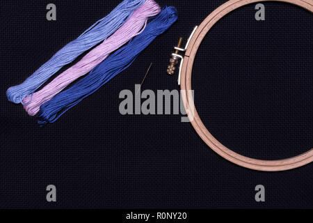 Tools for cross stitch. Threads, a hoop for embroidery and needle on a black canvas. Stock Photo