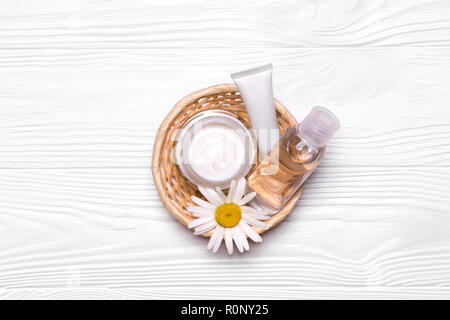 Bottles with cosmetics and chamomile flowers in a wicker basket. Cream, tonic, water and facial scrub. White tubes. Mockup natural cosmetic products. Stock Photo