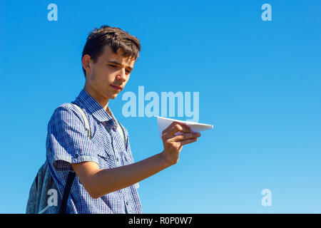 a young man on a blue sky holding a paper plane, the concept of flight and travel. Stock Photo