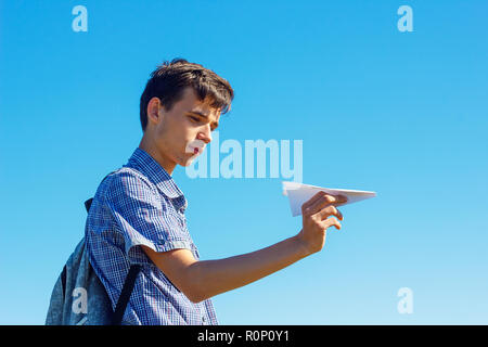a young man on a blue sky holding a paper plane, the concept of flight and travel. Stock Photo