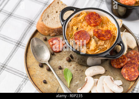 Slovak Christmas national cabbage soup in small black pot with sausage on old steel plate. Stock Photo