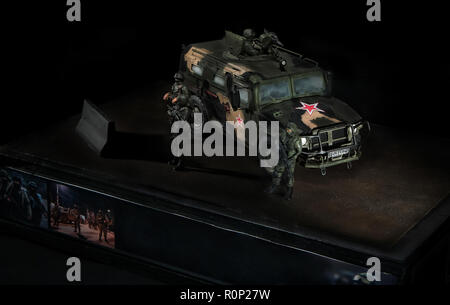 Model of the Russian Tiger fighting vehicle, with three soldiers nearby, on a curved stand. Black background Stock Photo