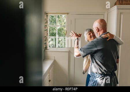 Happy elderly couple dancing together holding each other. Romantic senior couple having fun doing ballroom dancing at home. Stock Photo