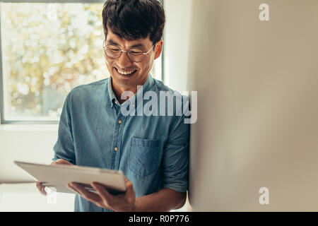 Man using tablet pc and smiling indoors. Man at home reading something funny on digital tablet. Stock Photo