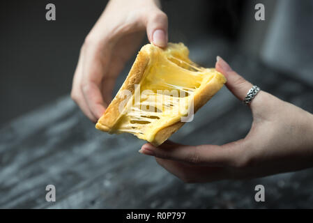 baked toast with stretched cheese in the hands of a woman Stock Photo