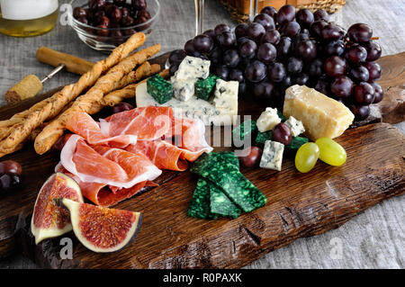 Dishes for a snack Antipasto on a wooden board with prosciutto, different kinds of cheese, grapes and figs on a table with wine Stock Photo