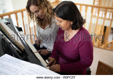 Latinx daughter and senior mother playing piano
