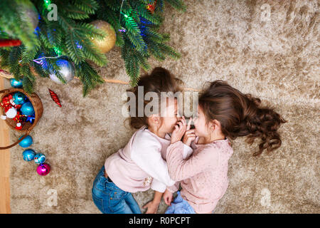 Christmas happy funny children sisters hugging and lying under the christmas tree Stock Photo