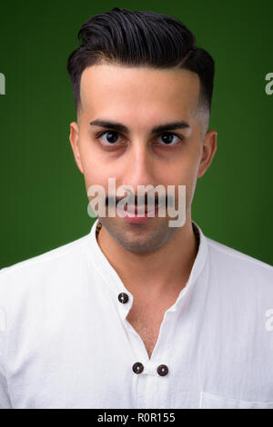 Young handsome Iranian man with mustache against green backgroun Stock Photo
