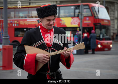 A man in a uniform of a Kuban Cossack plays a balalaika against a backdrop of the City Sightseeing tourist bus on Manezhnaya Square in Moscow, Russia Stock Photo