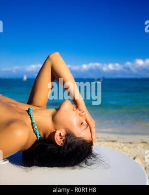 Portrait of young woman sunbathing, eyes closed, holding her head with hand, Caribbean sea, Guadeloupe, French West Indies, Stock Photo