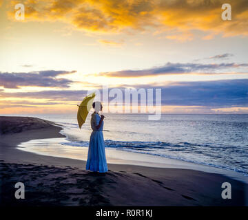 Young woman silhouette with long dress and umbrella facing the Caribbean sea at sunset, remote tropical beach, Guadeloupe, French West Indies, Stock Photo