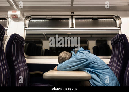 Man sleeping on train at night. UK Stock Photo
