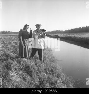 1940s outdoor life. A couple is out in the nature and is interested in plants and flowers. They are wearing the typical 1940s kind of outdoor clothes of sport character that is practical and durable. He is using binoculars to see better of something further ahead.  Sweden 1949. Photo Kristoffersson Ref AR30-3 Stock Photo