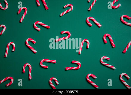 Above view of mini red and white candy canes displayed on a green paper background. Christmas sweets context. Minimal image. Stock Photo