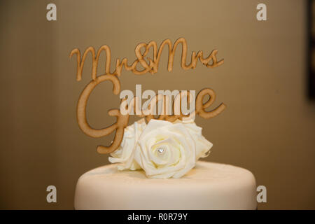 wooden cake topper of Mr and Mrs Grace with white rose flower on top tier of white iced round wedding cake at an English wedding Stock Photo