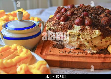 Chocolate cake with cherries, grated chocolate and whipped cream. Homemade cream puffs on festive table. Vintage sugar bowl. Close-up. Kitchen background Stock Photo