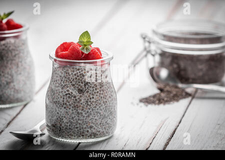 Closeup of served glass jars filled with sweet pudding of chia seeds and garnished with fresh raspberry and mint Stock Photo