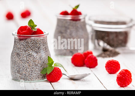 Closeup of served glass jars filled with sweet pudding of chia seeds and garnished with fresh raspberry and mint Stock Photo