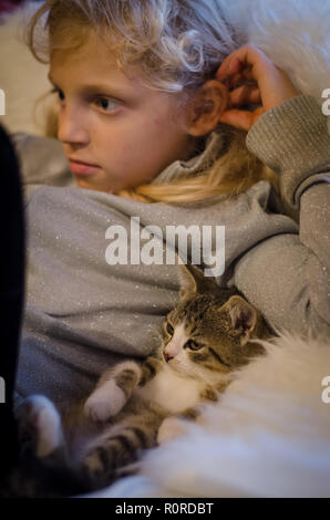 lovely blond girl and cute cat relaxing lying on sofa and watching television Stock Photo