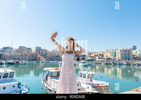 Traveling tourist woman on vacation in Heraklion Crete walking at the port. Lovely elegant girl takes selfies visiting the famous Mediterranean Veneti Stock Photo