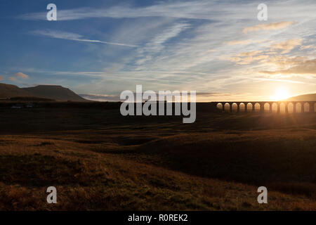A Northern rail class 158 sprinter train passing between Ribblehead viaduct and Ingleborough in the Yorkshire dales at sunset making a silhouette