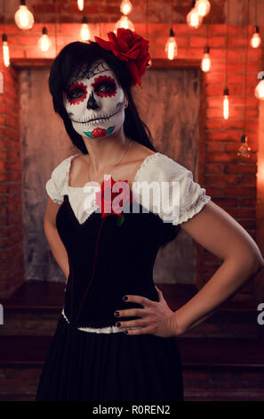 Photo of girl halloween with white make-up on her face, sewn on her mouth, black eyes on gloomy background of brick wall with burning lights Stock Photo