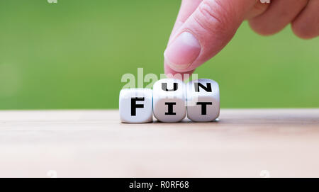 Hand is turning a dice and changes the word 'fit' to 'fun' Stock Photo