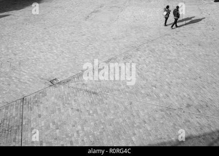 Blurred unrecognizable people from above walking on an open space square with shadows projecting on the floor Stock Photo