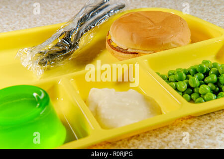 Elementary school lunch cheeseburger with mashed potatoes gelatin and green peas on portion tray Stock Photo