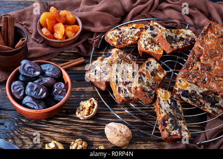 traditional chunky dried fruits cake loaf on a wire cake stand with brown cloth and ingredients on a rustic table, view from above, close-up Stock Photo