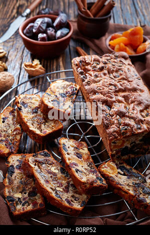 dried fruits rich cake on a wire cake stand with brown cloth, cinnamon sticks, dried apricots and date fruits on a rustic wooden table, vertical view  Stock Photo