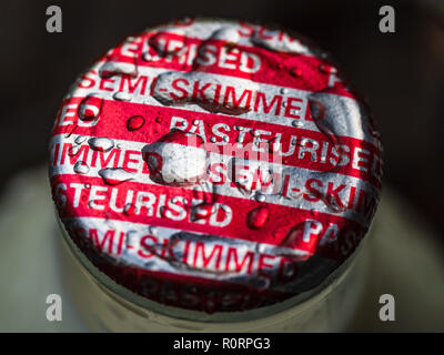 Milk Bottle Top - Semi Skimmed Pasteurised Red and Silver Milk Bottle top with raindrops pooled on top Stock Photo