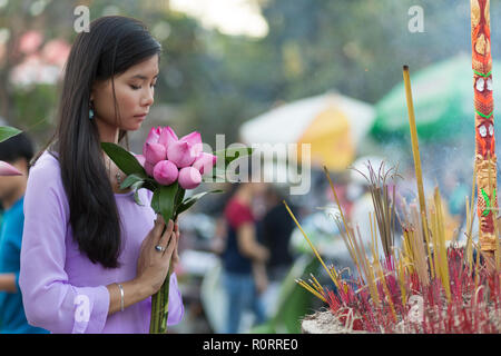 Peace and beauty in prayer as a young Vietnamese woman makes an offering of pretty fresh pink flowers at a Buddhist shrine with burning incense Stock Photo