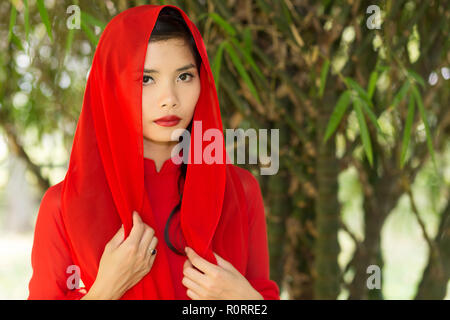 Pretty Vietnamese woman in a red head scarf standing with her hands to her chest looking at the camera with a serious expression Stock Photo