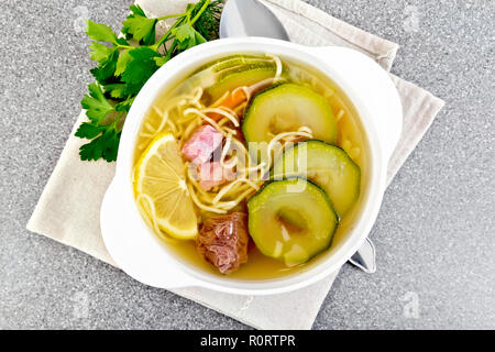 Soup with zucchini, beef, ham, lemon and noodles in a bowl on a napkin, parsley and dill on a granite table background on top Stock Photo