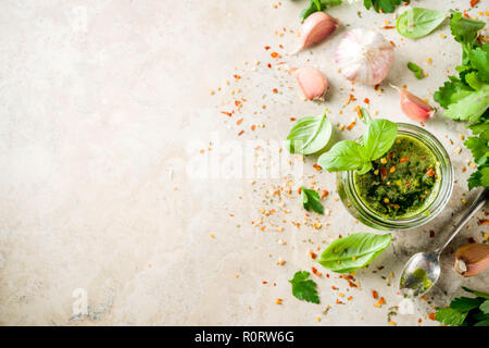 Argentinian traditional food, raw homemade green Chimichurri salsa or sauce woth parsley, garlic, basil leaves, hot pepper and spices, light stone tab Stock Photo