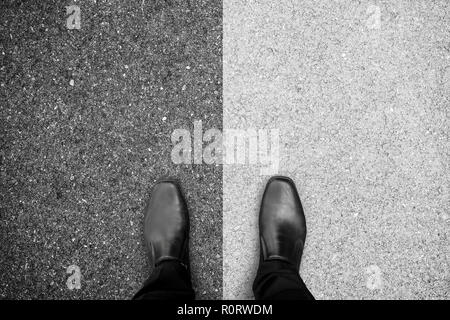 Businessman in black shoes standing between black and white concrete floor representing right and wrong, darkness and brightness. Stock Photo