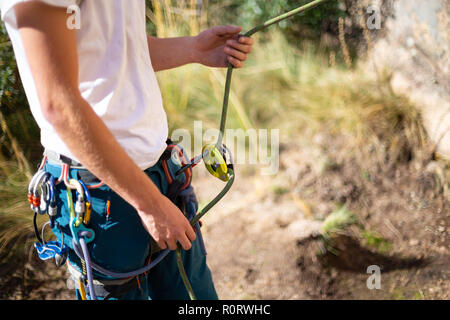 Crop side view of man wearing special equipment securing climbing partners standing in sunlight Stock Photo