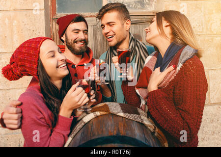 Smiling european men and women during party photoshoot. The guys posing as friends at studio fest with wineglasses with hot mulled wine on foreground. Stock Photo