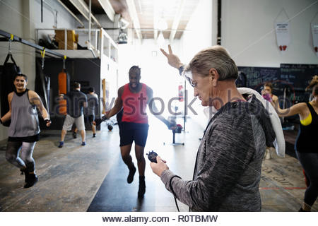 Trainer with stopwatch timing male boxers jump roping in gym