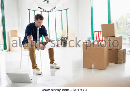 Businessman with laptop and blueprints in new, empty office space with cardboard boxes