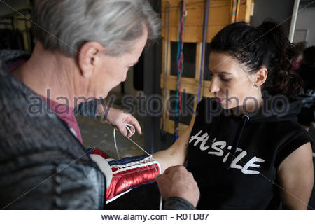 Trainer helping female boxer lacing boxing gloves in gym
