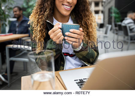 Woman drinking coffee, working at laptop on cafe patio