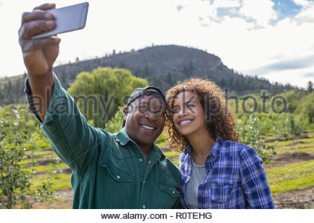 Father and daughter farmers taking selfie with camera phone in orchard