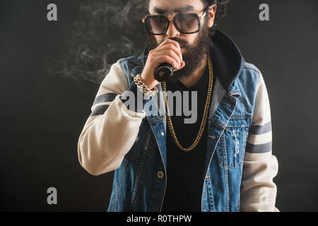 Young man with beard and sunglasses vaping an electronic cigarette. Vaper hipster smoke vaporizer Stock Photo