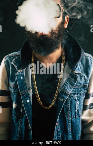 Young man with beard throwing a cloud of steam. Black background. Vaping an electronic cigarette with a lot of smoke Stock Photo