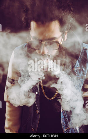 Young man with beard throwing a cloud of steam. Black background. Vaping an electronic cigarette with a lot of smoke Stock Photo